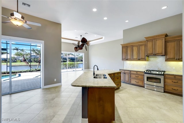 kitchen featuring a kitchen island with sink, sink, a tray ceiling, tasteful backsplash, and stainless steel gas range