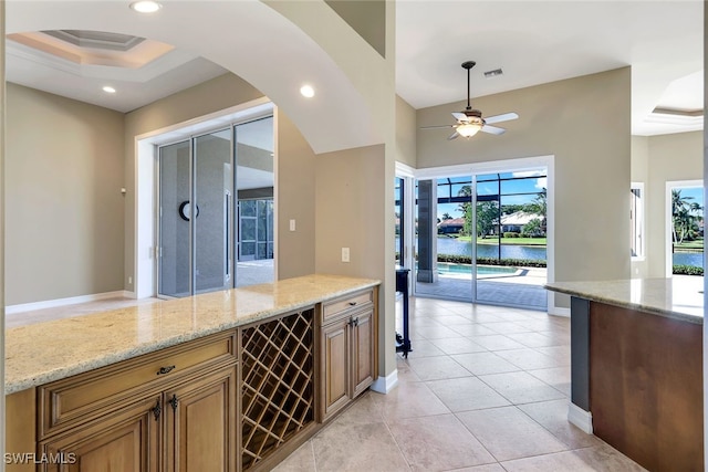 kitchen featuring ceiling fan, a water view, light stone counters, and light tile patterned floors