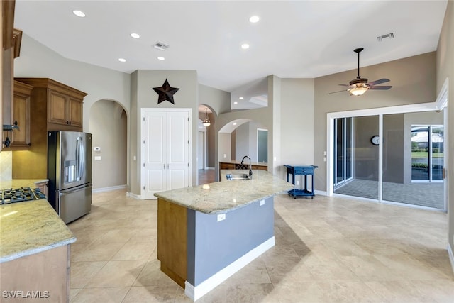 kitchen with an island with sink, sink, light stone countertops, and stainless steel appliances