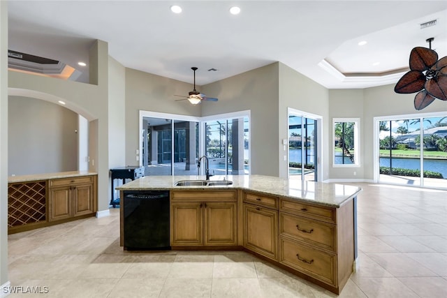 kitchen featuring a center island with sink, sink, light stone counters, a water view, and dishwasher