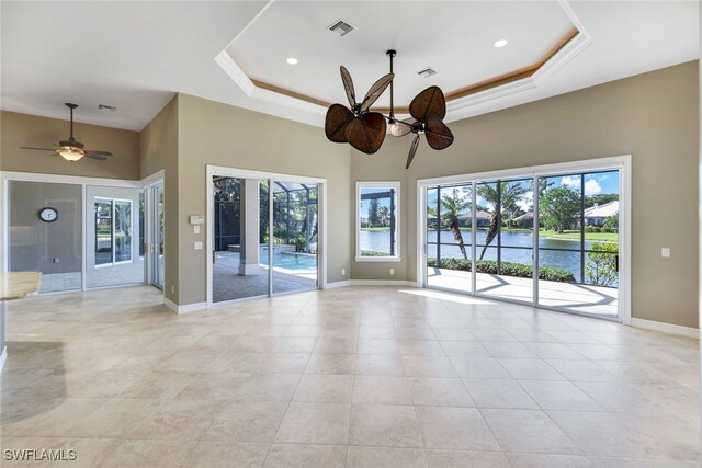 empty room with ceiling fan, a water view, a raised ceiling, and a wealth of natural light