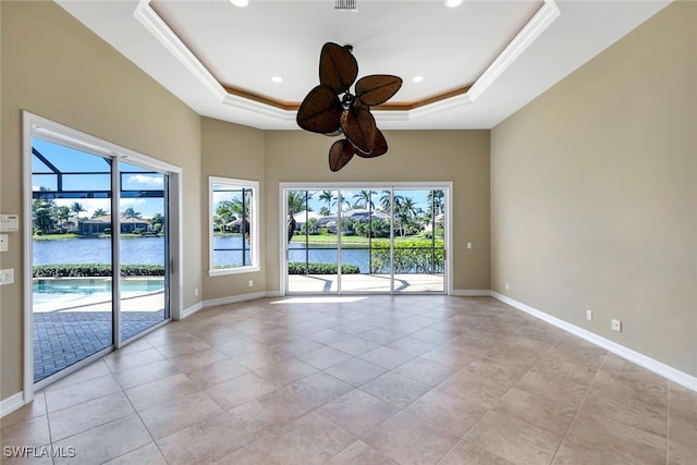 empty room featuring a tray ceiling, a water view, ornamental molding, and ceiling fan