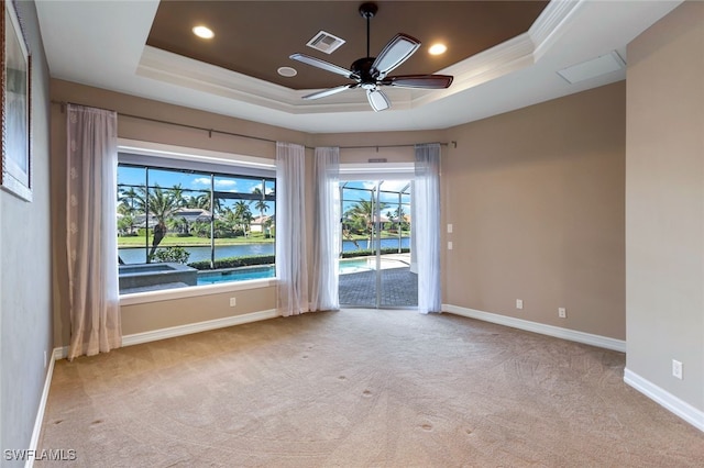 empty room with light carpet, a water view, ceiling fan, and a raised ceiling