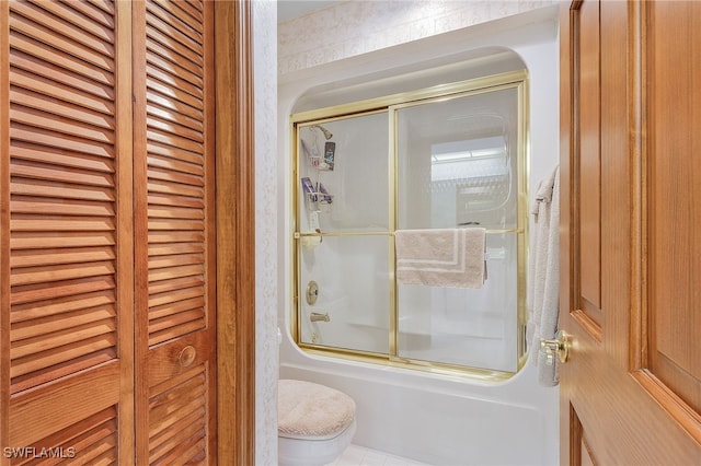 bathroom featuring tile patterned flooring, combined bath / shower with glass door, and toilet