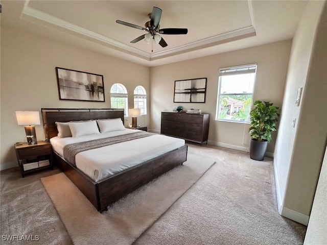 bedroom featuring ceiling fan, light colored carpet, ornamental molding, and a tray ceiling