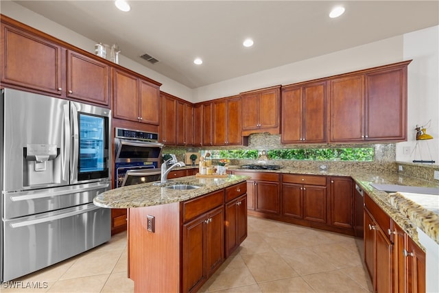 kitchen featuring light stone countertops, sink, appliances with stainless steel finishes, and an island with sink