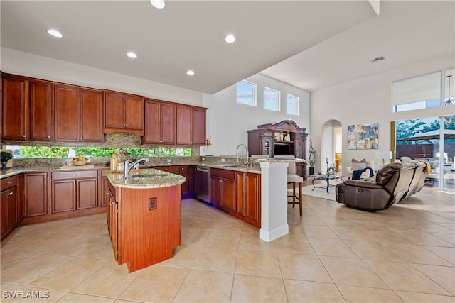 kitchen with light stone countertops, sink, an island with sink, a breakfast bar area, and light tile patterned flooring