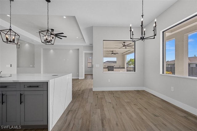 unfurnished dining area featuring light wood-type flooring, a raised ceiling, ceiling fan, and sink