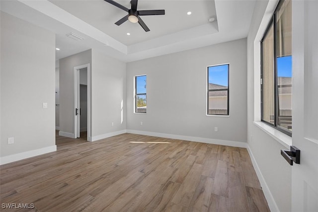 spare room featuring a tray ceiling, ceiling fan, and light hardwood / wood-style floors