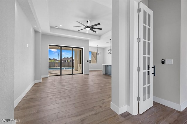 unfurnished living room with french doors, wood-type flooring, and ceiling fan with notable chandelier