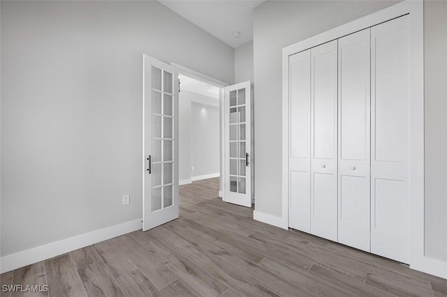 unfurnished bedroom featuring a closet, french doors, and light wood-type flooring