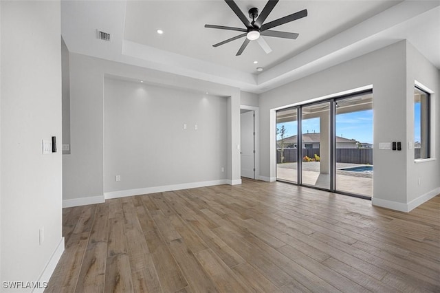 unfurnished room featuring ceiling fan, light hardwood / wood-style floors, and a tray ceiling