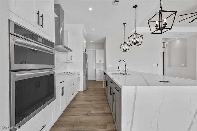 kitchen featuring a large island, sink, wall chimney range hood, white cabinets, and appliances with stainless steel finishes