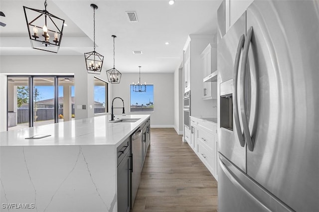 kitchen featuring a large island with sink, stainless steel appliances, hanging light fixtures, and sink