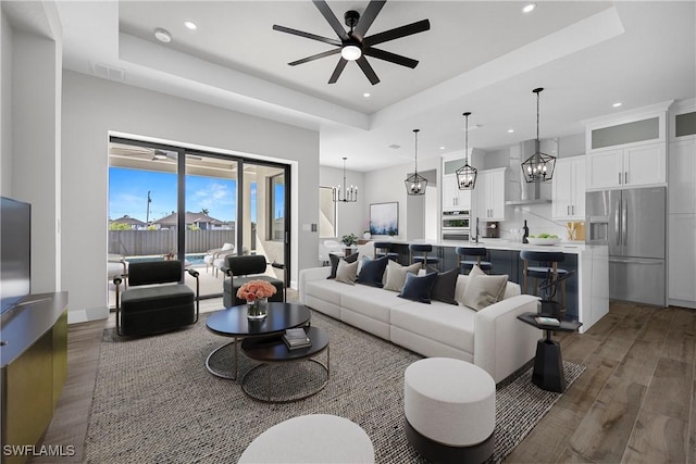 living room with dark hardwood / wood-style floors, ceiling fan, and a tray ceiling