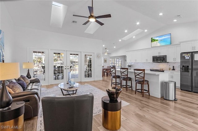 living room with french doors, light hardwood / wood-style floors, high vaulted ceiling, and a wealth of natural light