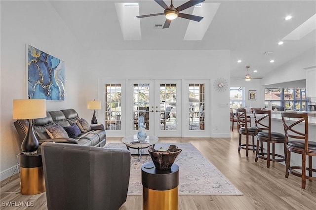 living room with high vaulted ceiling, french doors, a skylight, ceiling fan, and light hardwood / wood-style floors