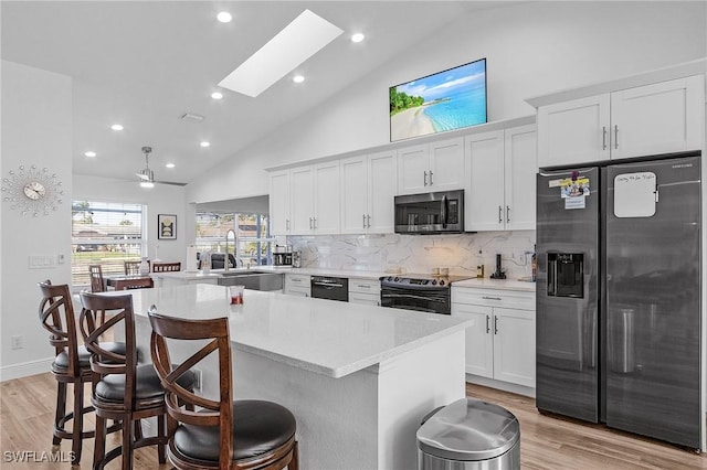 kitchen featuring a skylight, stainless steel appliances, sink, white cabinets, and light hardwood / wood-style floors