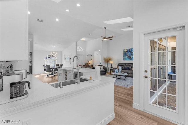 kitchen featuring sink, hanging light fixtures, light hardwood / wood-style flooring, vaulted ceiling with skylight, and ceiling fan with notable chandelier