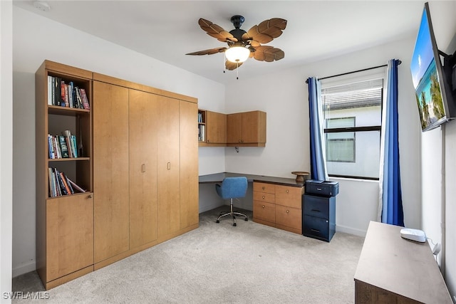 home office with built in desk, ceiling fan, and light colored carpet