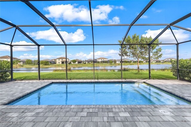 view of pool with a patio, a water view, glass enclosure, and a lawn