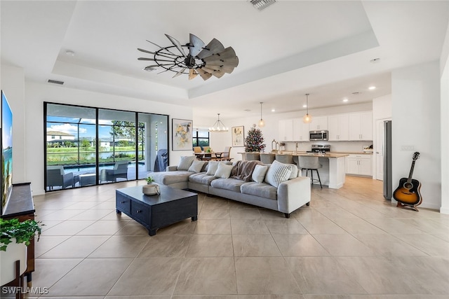 living room featuring ceiling fan with notable chandelier, a wealth of natural light, and a raised ceiling