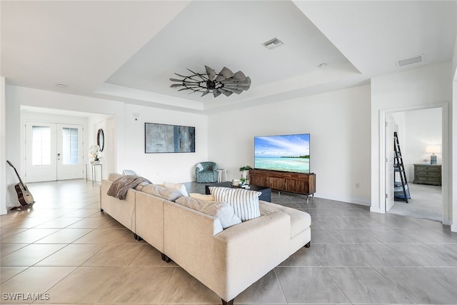 tiled living room featuring ceiling fan, french doors, and a raised ceiling