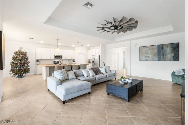 living room with ceiling fan, a raised ceiling, and light tile patterned floors