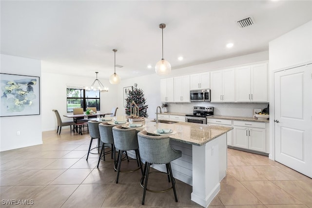 kitchen with pendant lighting, tasteful backsplash, white cabinetry, an island with sink, and stainless steel appliances