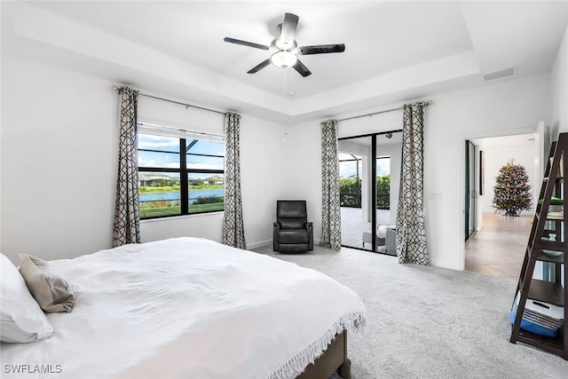 bedroom featuring a water view, a tray ceiling, ceiling fan, and access to outside