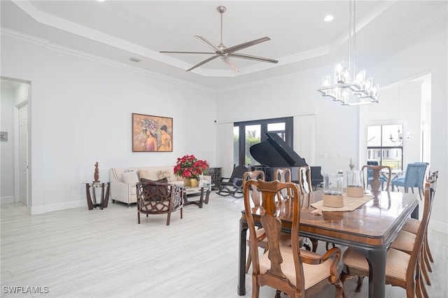 dining space with ceiling fan with notable chandelier, a tray ceiling, light hardwood / wood-style flooring, and crown molding