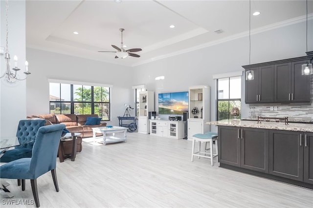 living room featuring ceiling fan with notable chandelier, a wealth of natural light, and a tray ceiling