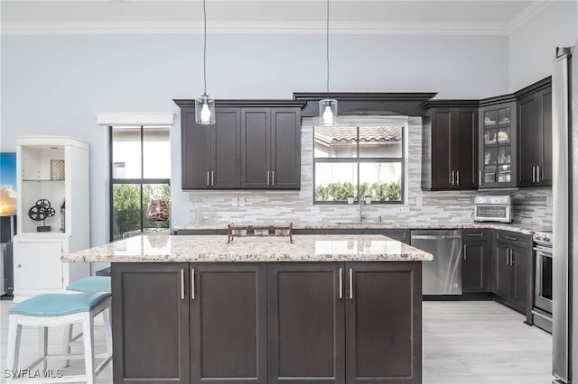 kitchen with hanging light fixtures, stainless steel appliances, a wealth of natural light, and a center island with sink