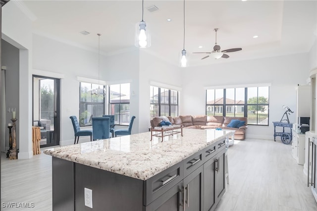 kitchen featuring light stone countertops, ceiling fan, a high ceiling, a kitchen island, and light wood-type flooring