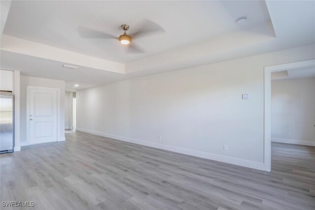 unfurnished room featuring light wood-type flooring, ceiling fan, and a tray ceiling