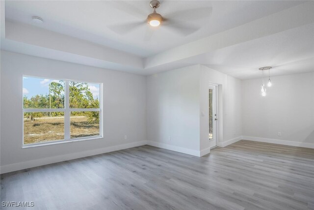 spare room with ceiling fan, a raised ceiling, and light wood-type flooring