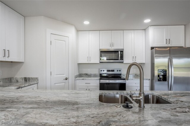 kitchen with white cabinets, light stone countertops, appliances with stainless steel finishes, and sink