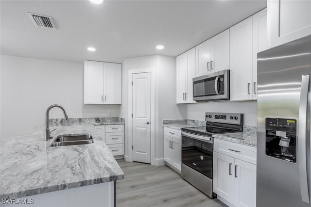 kitchen featuring appliances with stainless steel finishes, sink, white cabinets, light wood-type flooring, and light stone counters