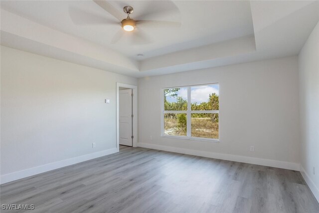 empty room with ceiling fan, light hardwood / wood-style flooring, and a raised ceiling