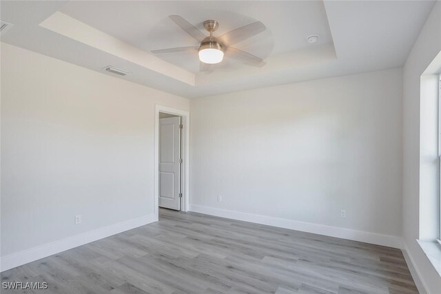 unfurnished room featuring light hardwood / wood-style floors, plenty of natural light, ceiling fan, and a raised ceiling