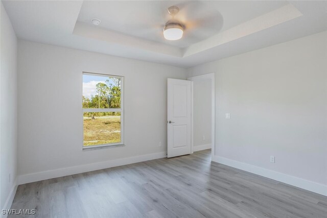 empty room with ceiling fan, a tray ceiling, and light wood-type flooring