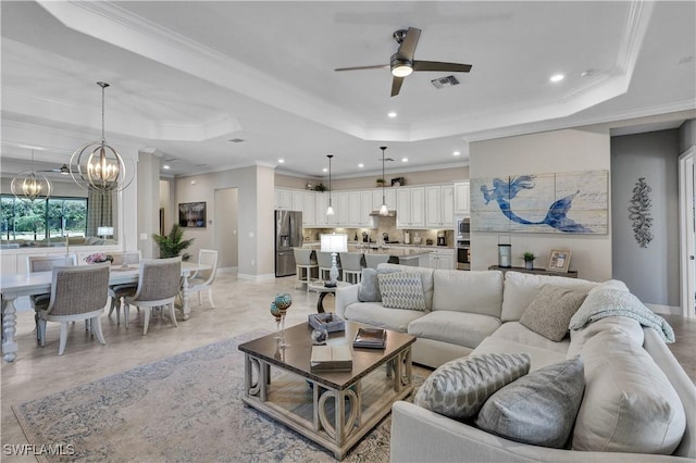 living room with a tray ceiling, crown molding, and ceiling fan with notable chandelier