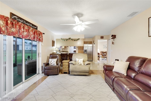 living room featuring ceiling fan, light hardwood / wood-style flooring, and a textured ceiling