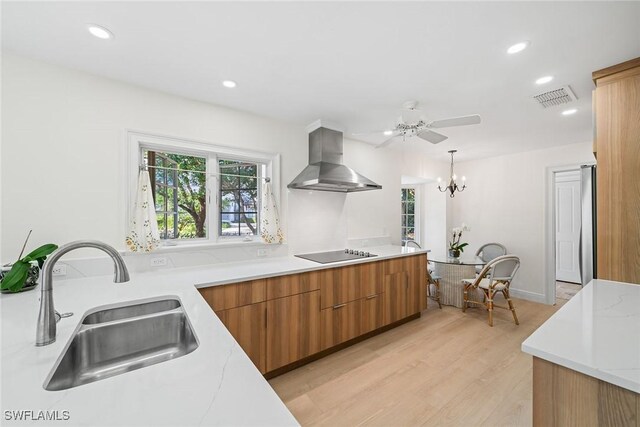 kitchen with wall chimney range hood, sink, hanging light fixtures, stainless steel fridge, and light hardwood / wood-style floors