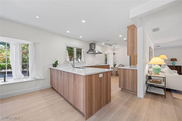 kitchen with kitchen peninsula, light hardwood / wood-style floors, plenty of natural light, and wall chimney range hood