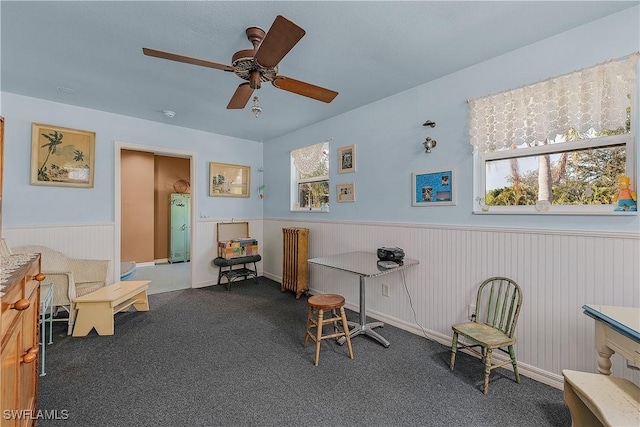 interior space featuring ceiling fan, dark carpet, and radiator heating unit