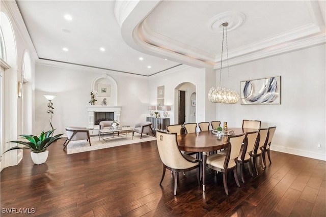 dining space featuring dark hardwood / wood-style floors, a raised ceiling, ornamental molding, and a notable chandelier