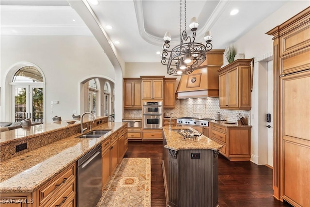 kitchen featuring sink, stainless steel appliances, dark wood-type flooring, light stone counters, and a large island with sink