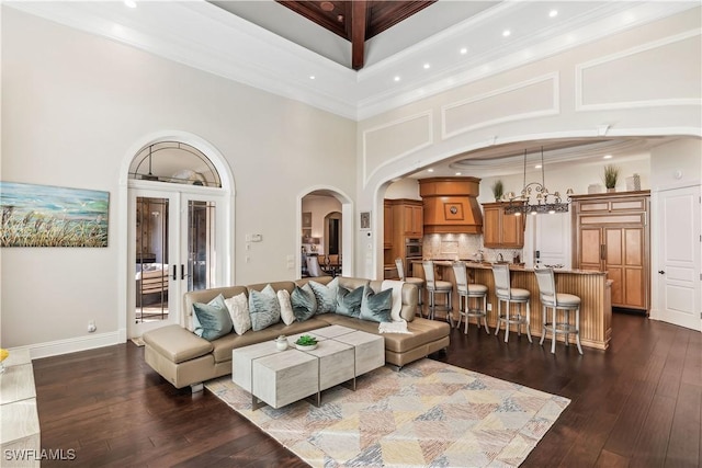 living room with french doors, a high ceiling, dark hardwood / wood-style flooring, a notable chandelier, and crown molding