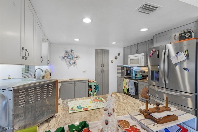 kitchen featuring gray cabinets, light stone countertops, kitchen peninsula, and appliances with stainless steel finishes